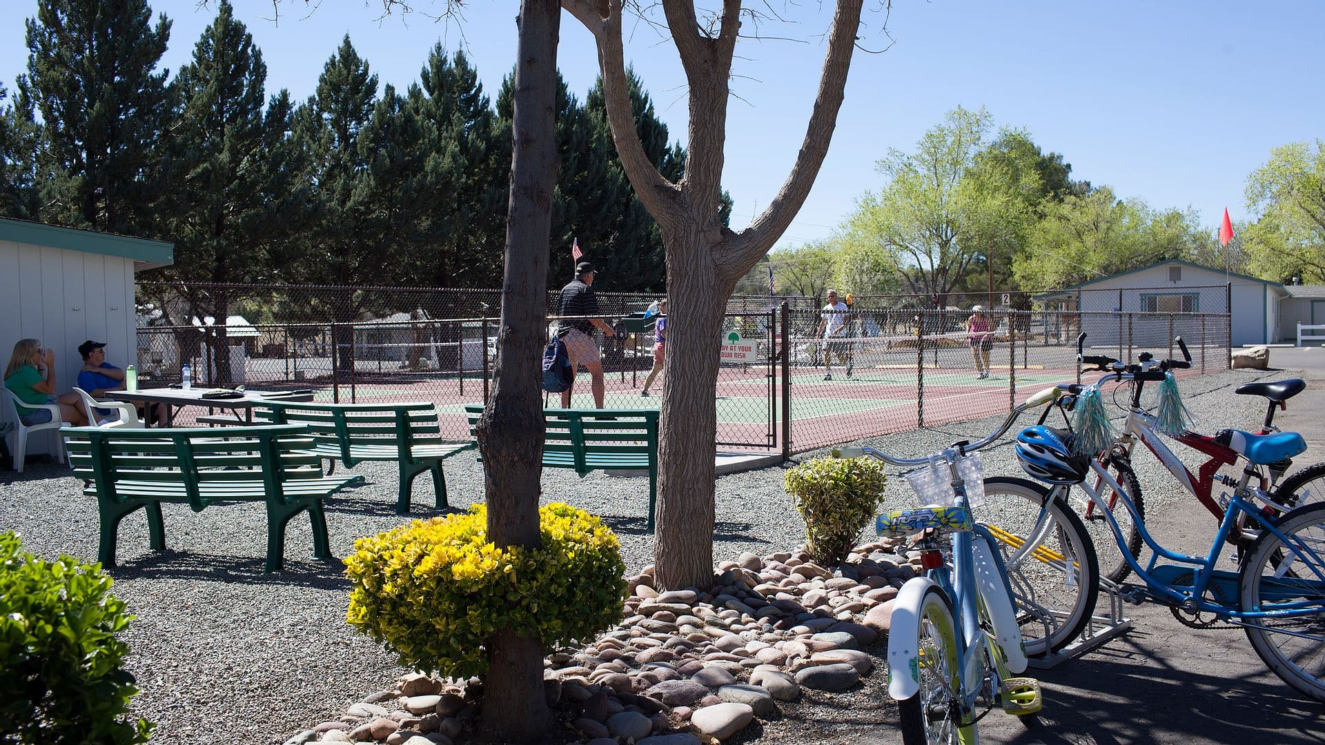 Residents playing on the court at Orchard Ranch RV Resort, with shaded benches and bike racks alongside.
