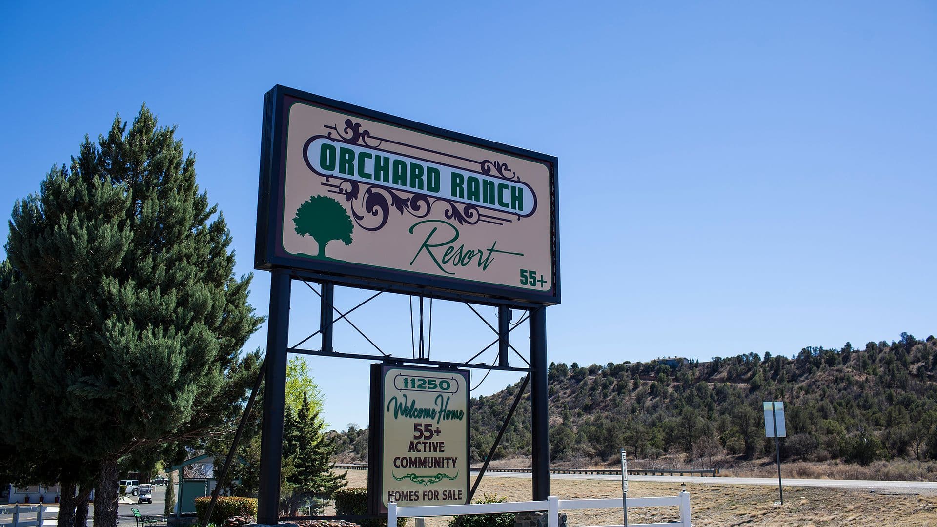 The Old West-style welcome entrance at Orchard Ranch RV Resort with Arizona's high-country hills beyond.